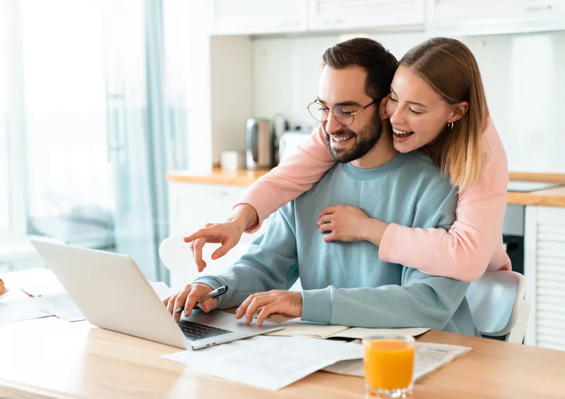 Couple souriant consultant leur investissement immobilier sur un ordinateur